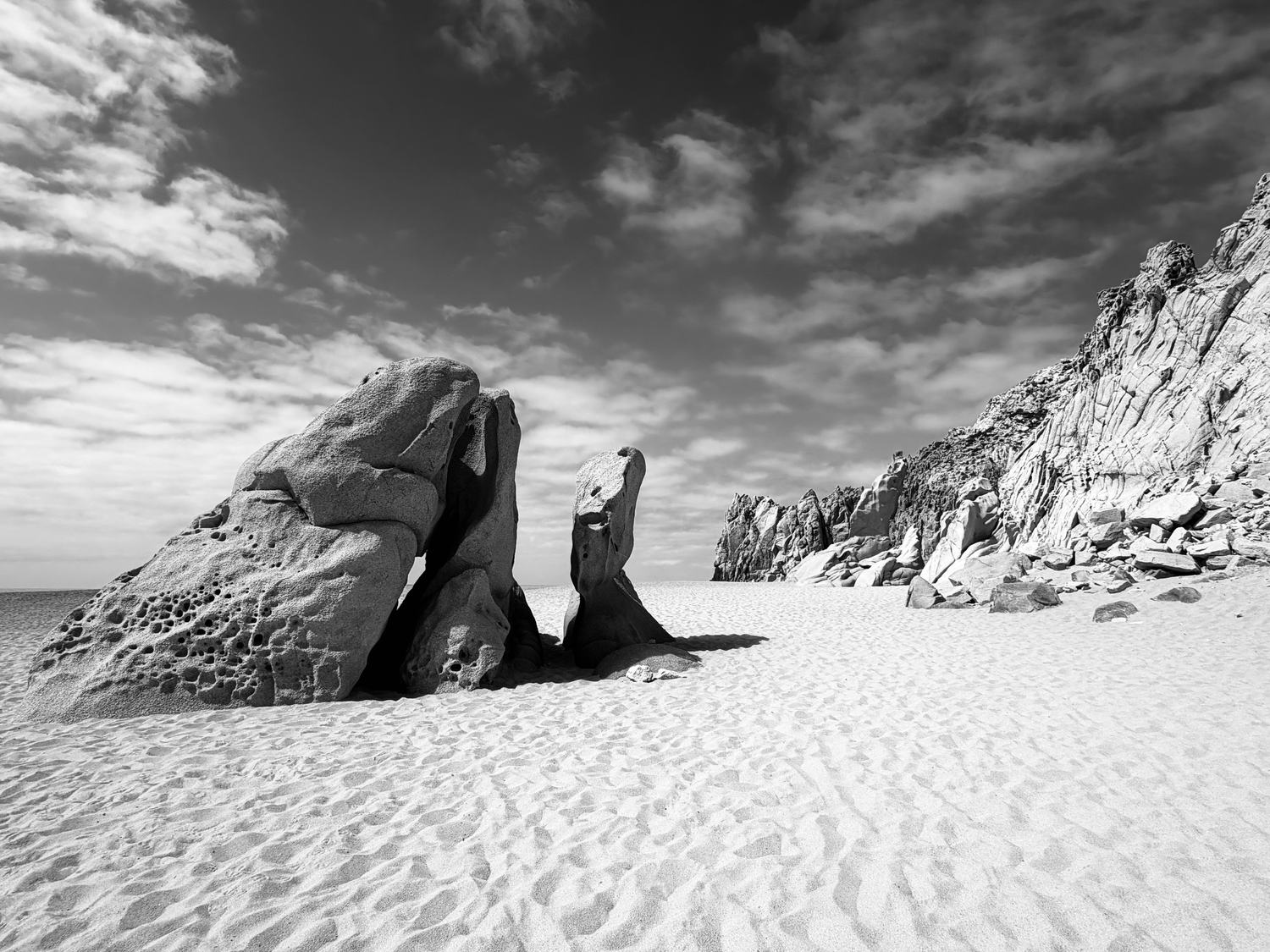 Wind-eroded granite boulders on white sand under a hard midday sky.